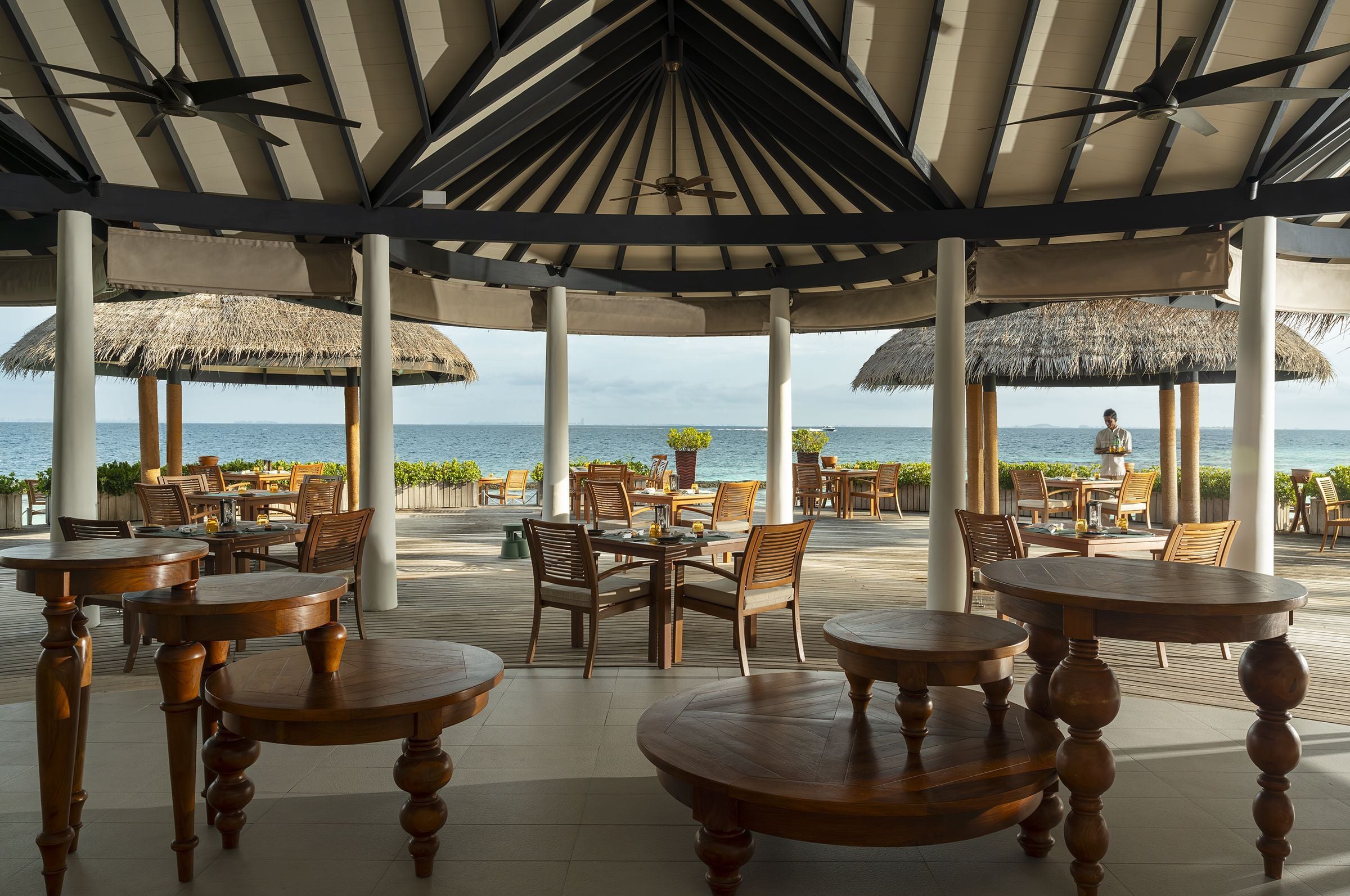 Dining tables under the thatched roof of Cayenne Grill, looking out to the lagoon