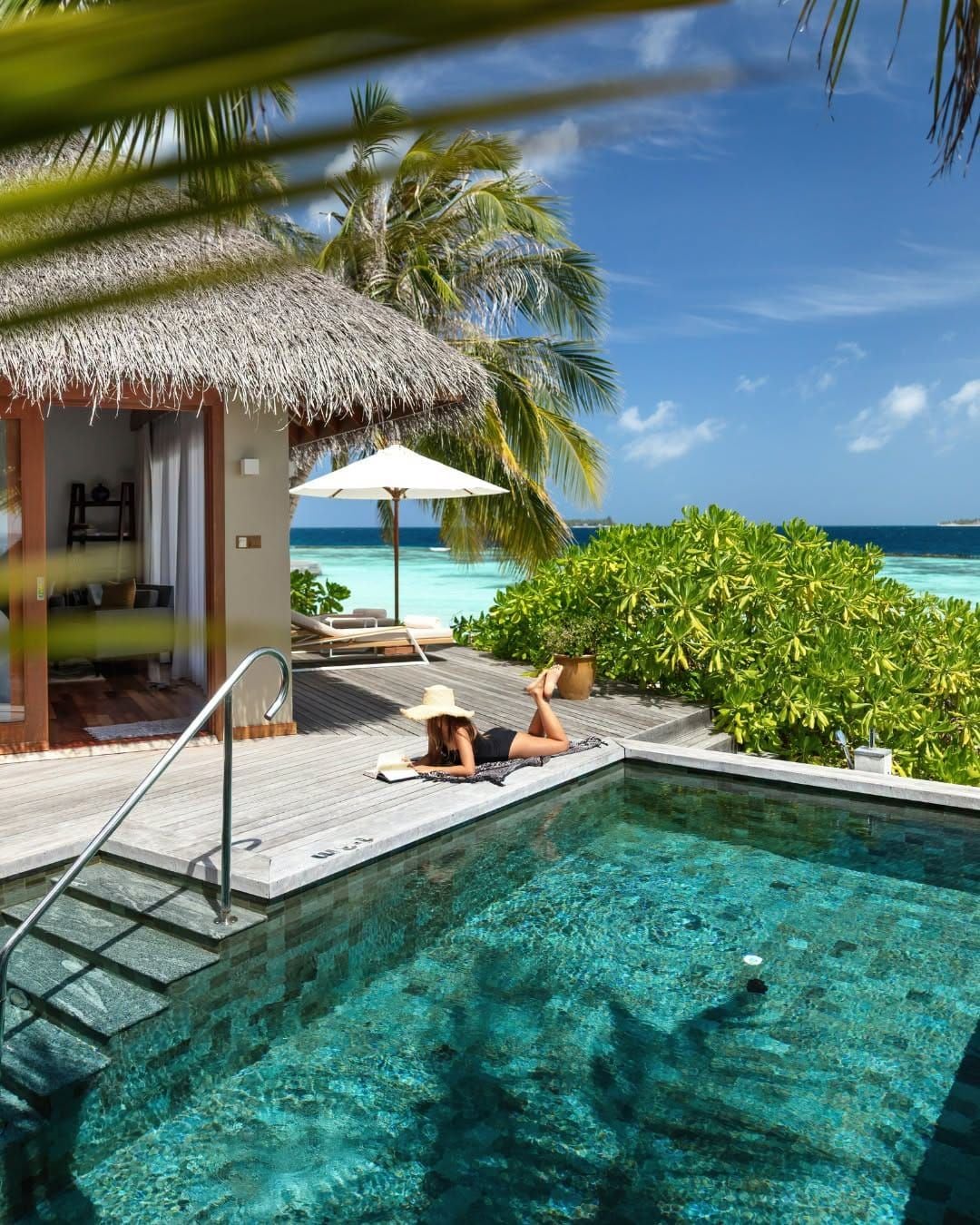 Private plunge pool and sun deck beside a thatched beach villa, with the sea beyond