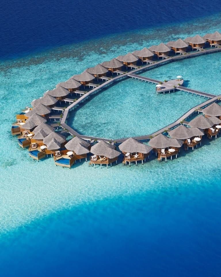 Aerial view of the curving arc of overwater villas on a blue lagoon