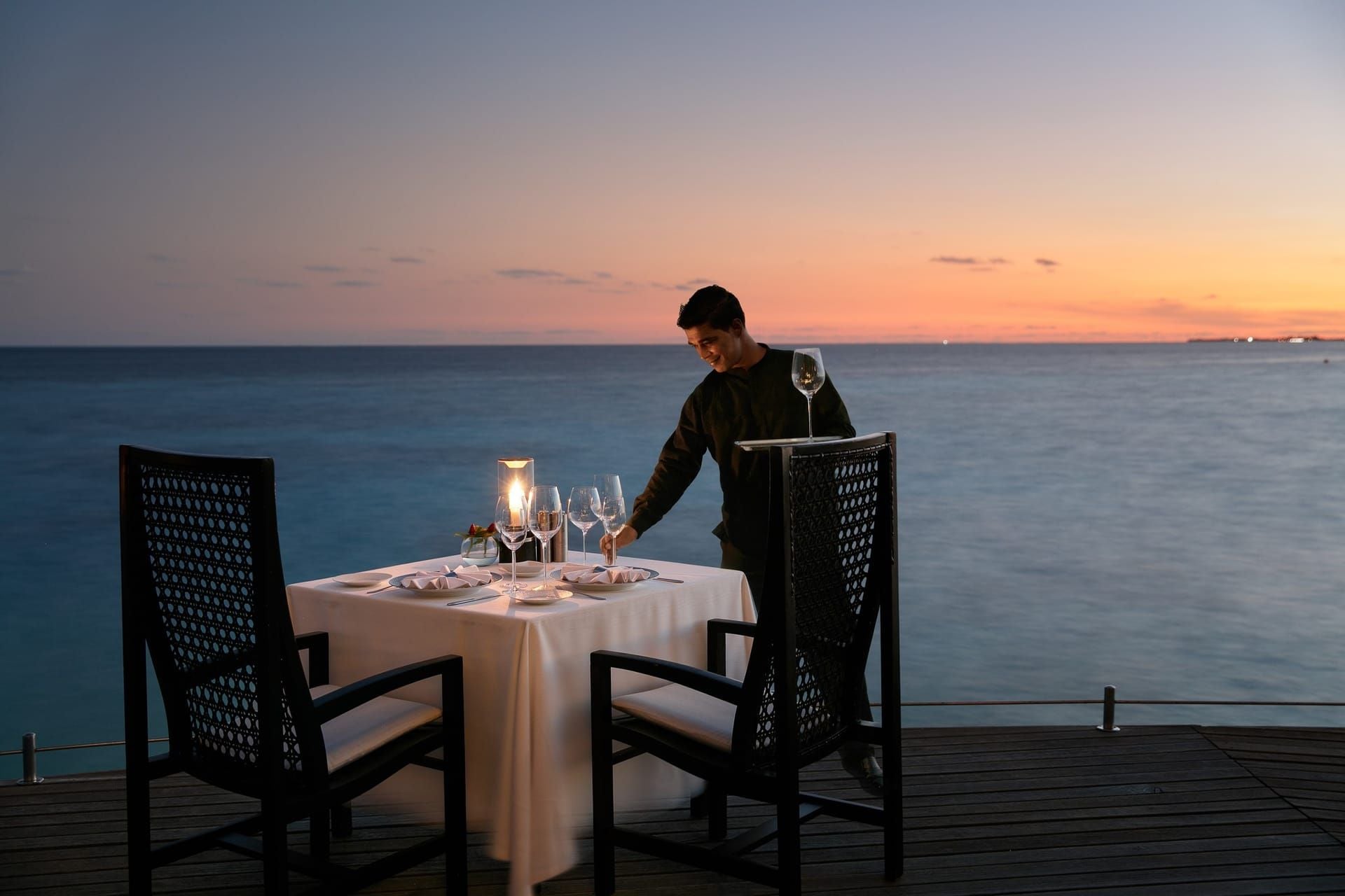 Waiter preparing a candlelit table for two by the sea at sunset