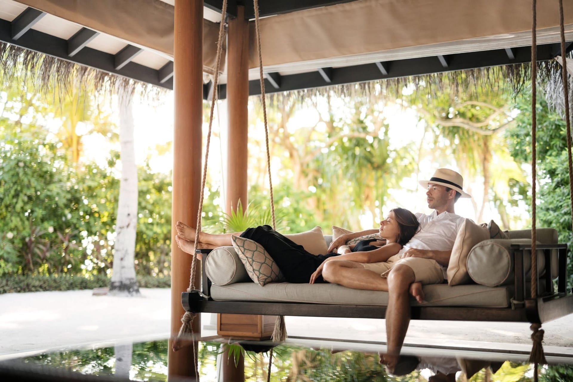 Couple relaxing on a hanging swing daybed in a shaded garden pavilion